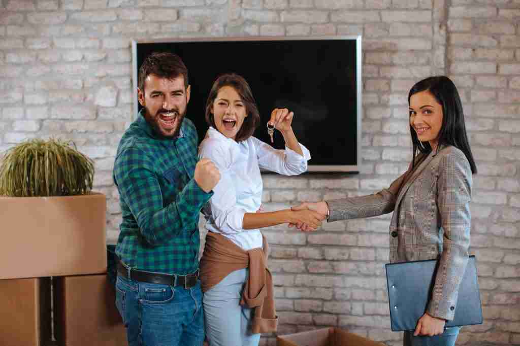 Young couple shaking hands with real estate agent and showing the keys of a new home