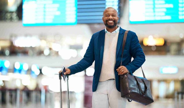 Portrait of black man, airport and smile with luggage and flight schedule display for business trip